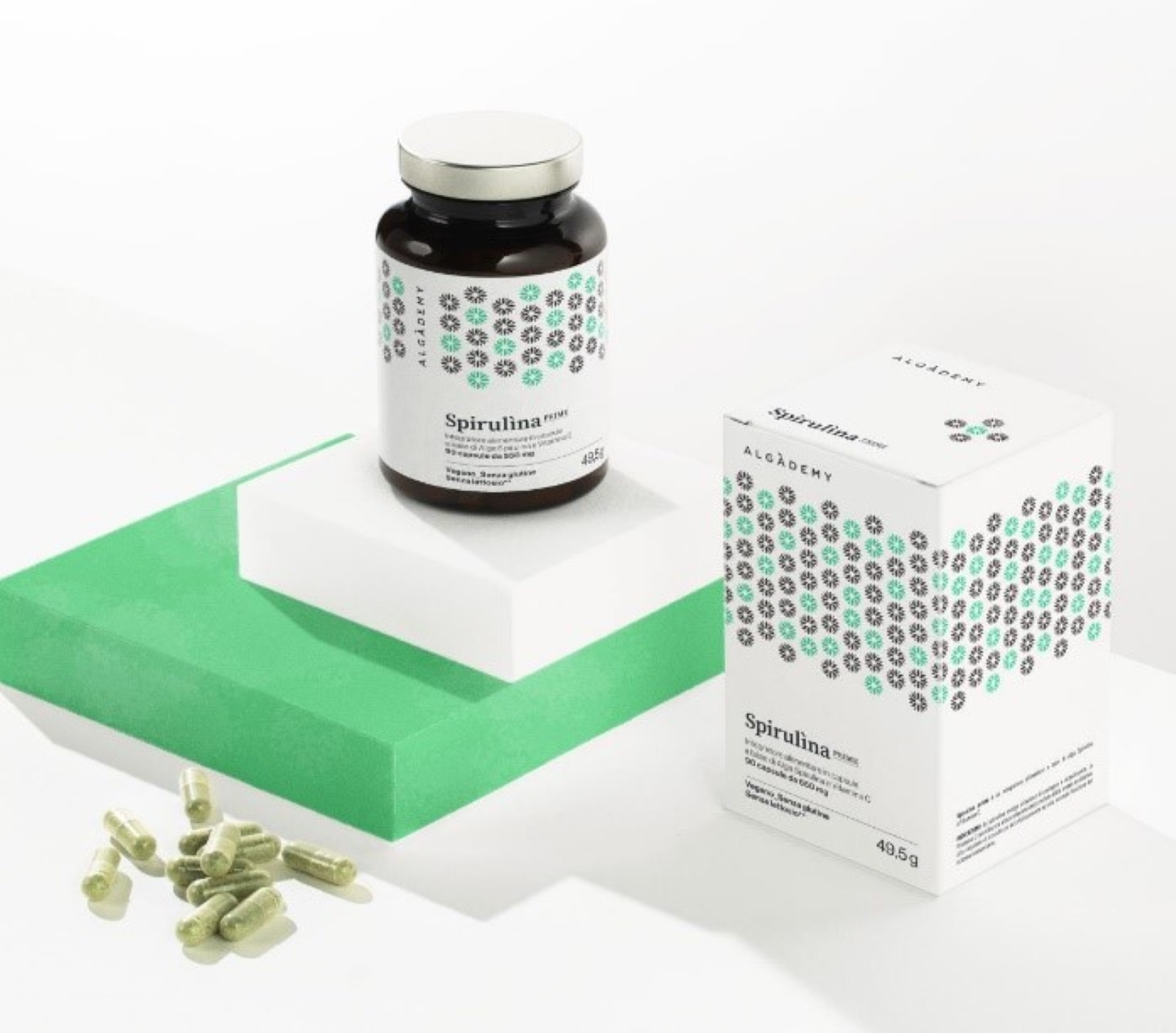 Glasflasche mit Spirulina-Kapseln und Verpackung auf einer grünen Fläche, daneben liegen einige Kapseln.